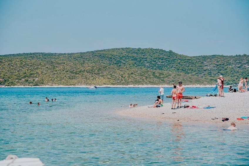 A beach with people swimming and sunbathing, a boat in the water, and a green hillside in the background. 3