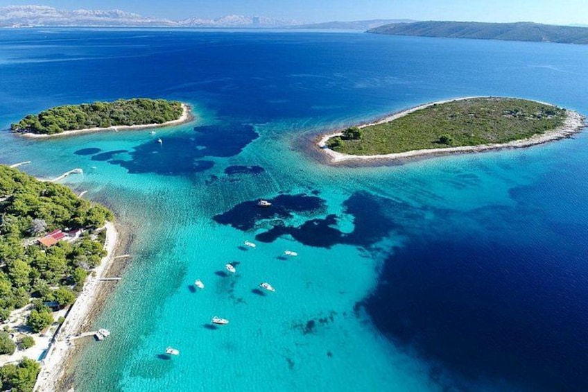 Een kustgebied met helder turquoise water, kleine eilandjes en boten die vlakbij de kust liggen aangemeerd. 4