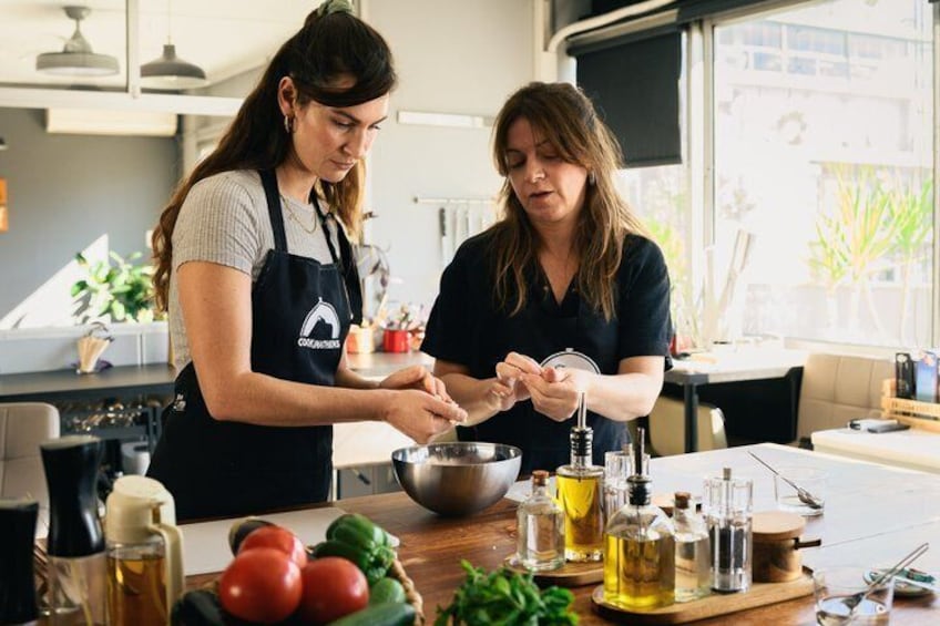 Twee personen bereiden eten in een keuken, met groenten, kookolie en keukengerei in beeld. 1