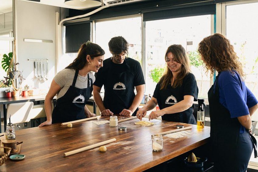 A group of people wearing aprons working at a wooden table with cooking utensils and ingredients. 2