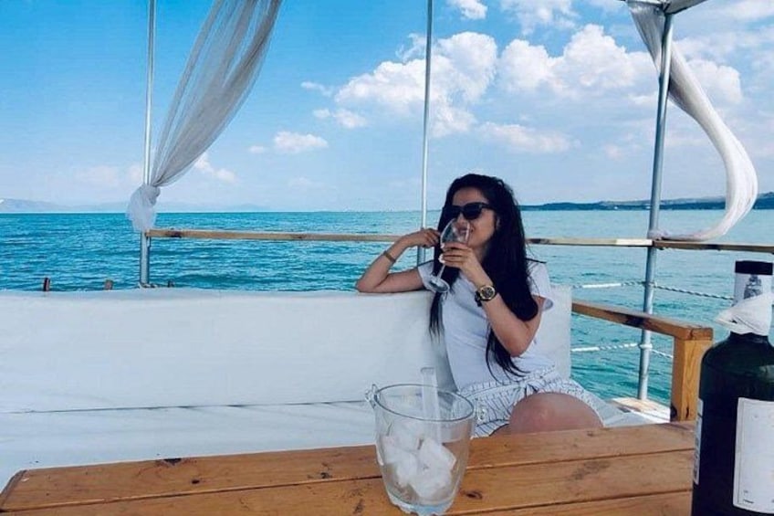 A person sitting at a wooden table by the sea, holding a glass. 4
