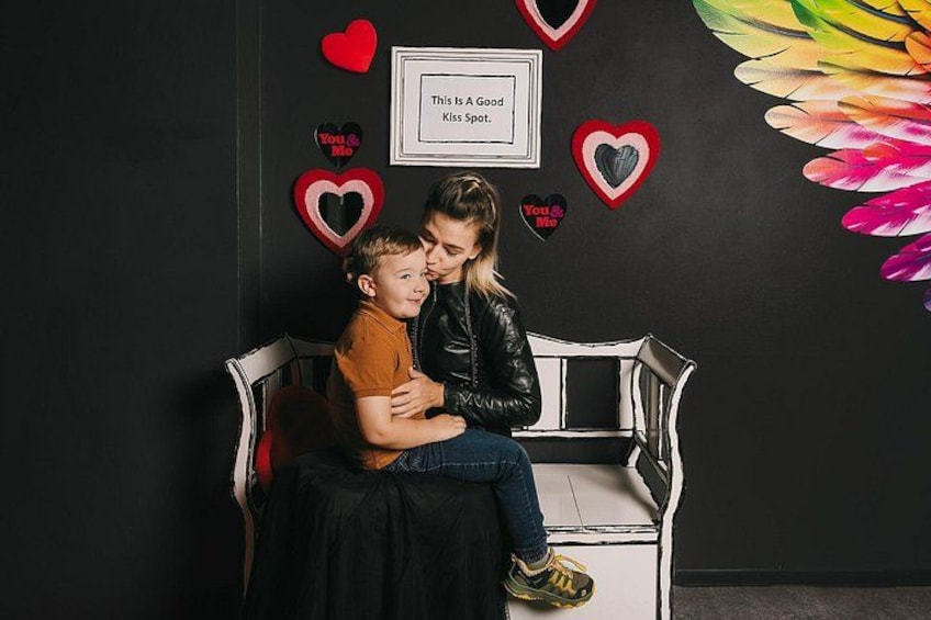 Iemand zit op een bankje, samen met een kind, omringd door hartvormige decoraties en een lijst met een bordje. 4