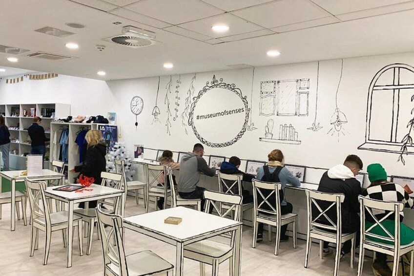 Een museumcafé met mensen aan tafels, een witte muur met tekeningen en een kerstboom. 3