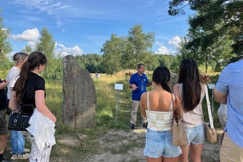 Un gruppo di persone in piedi vicino a una grande formazione rocciosa, probabilmente un monumento naturale, mentre una guida o un oratore si rivolge a loro. 2
