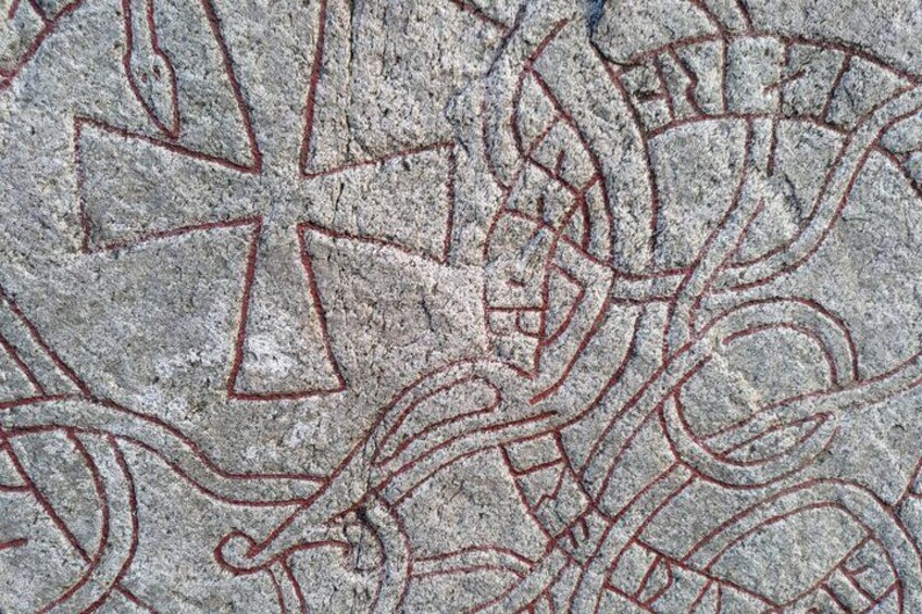 A stone surface with etched patterns, including a prominent cross and abstract designs. 2