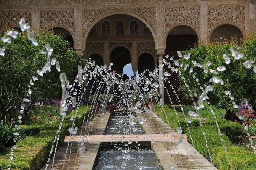 A water fountain with multiple streams in a garden with ornate architecture in the background. 4