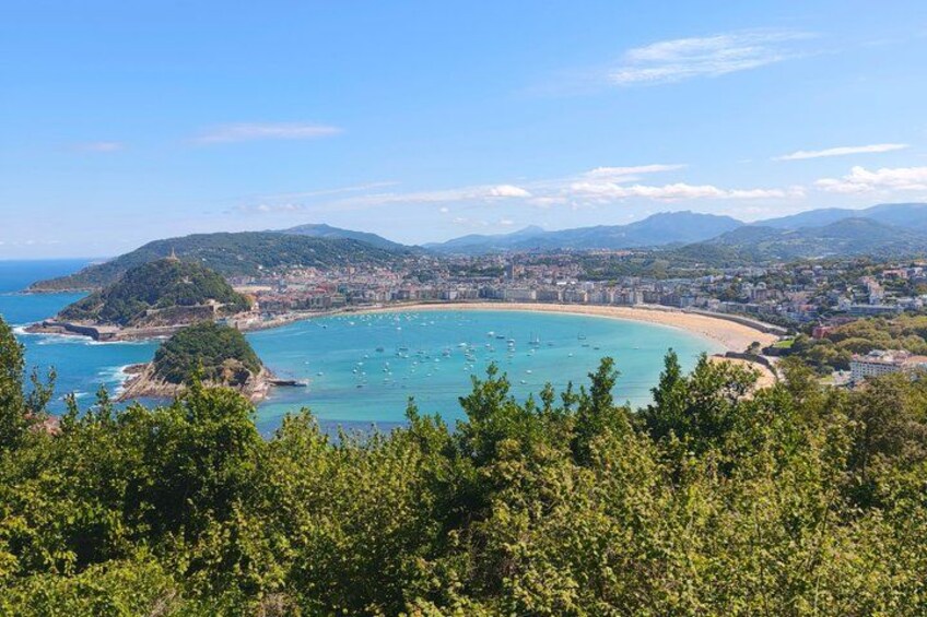 A coastal landscape with a bay, a beach, and a forested hill. 5