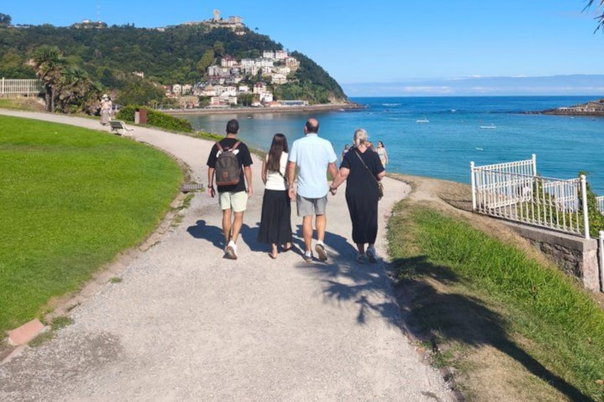 A group of people walking on a coastal path with a view of the sea and a hill with buildings in the background. 2