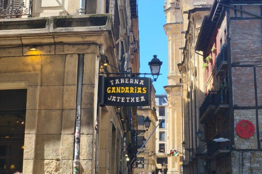 A narrow street with a sign for 'Taberna Gandarias' and a traditional European building. 4
