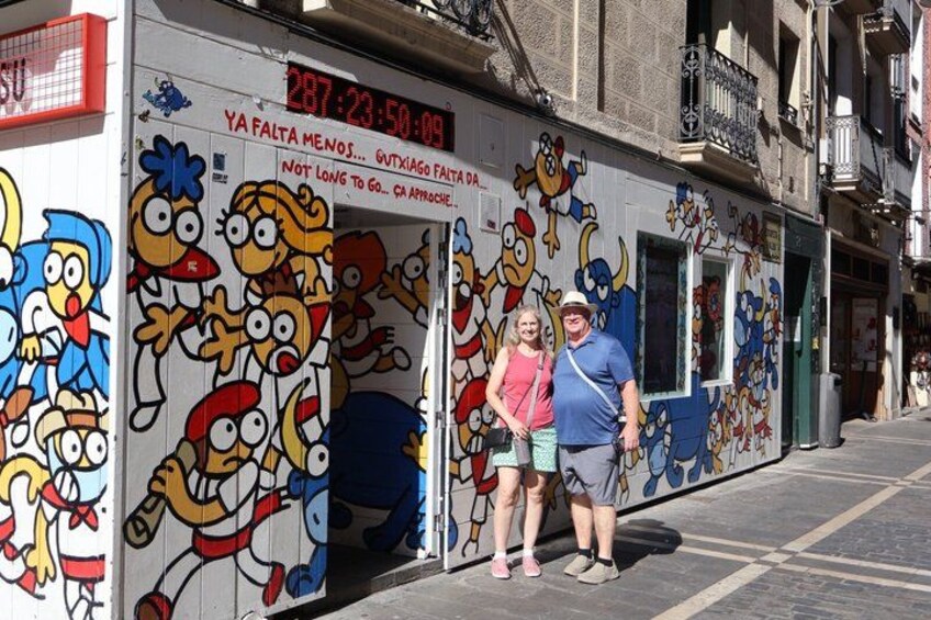 A street with a mural of cartoon characters, a digital clock, and a building with balconies. 4