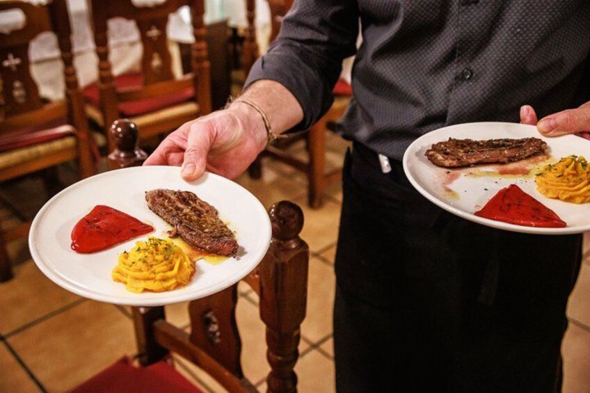 A person holding a plate with a steak, a red sauce, and a yellow side dish. 2