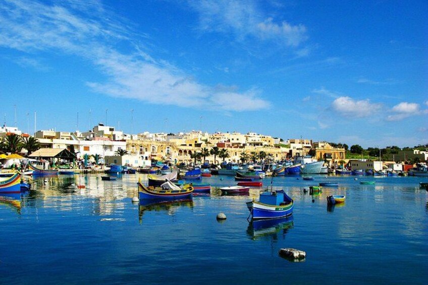 A harbor with numerous colorful boats, a calm blue sea, and a coastal town with buildings in the background. 1