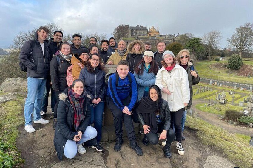 A group of people posing in front of a historic building with a cemetery in the background. 2