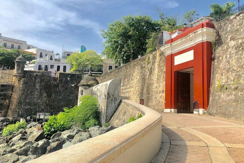 A stone wall with a curved pathway leading to a red entrance. 2