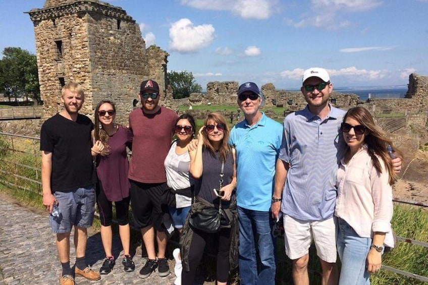 A group of people standing in front of a stone ruin with a tower, on a cobblestone path. 2