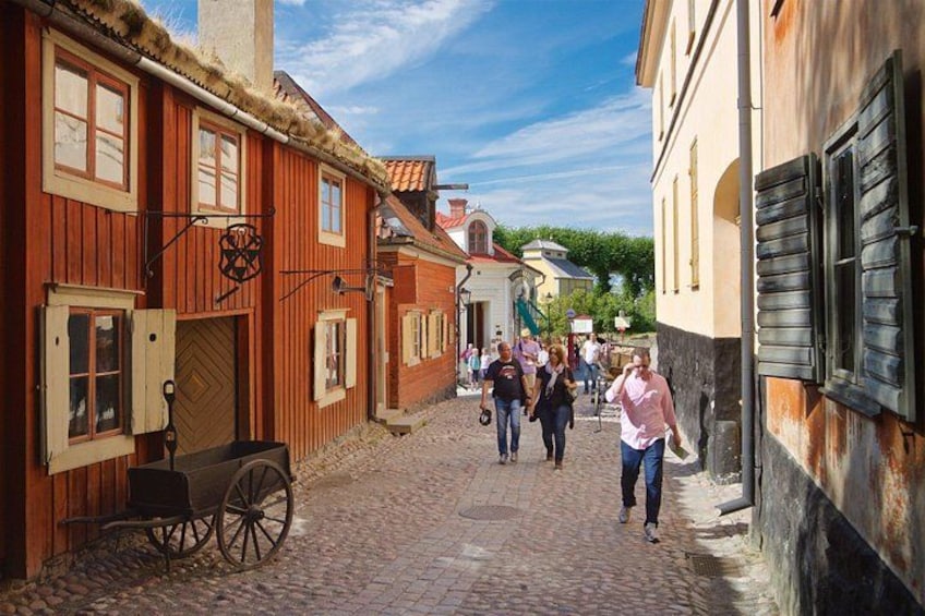 A cobblestone street lined with historic buildings, a wooden cart, and pedestrians. 4