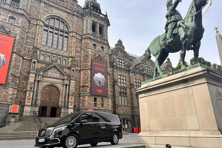 Un edificio histórico con una estatua ecuestre, un gran cartel y un coche negro estacionado en la fachada. 1
