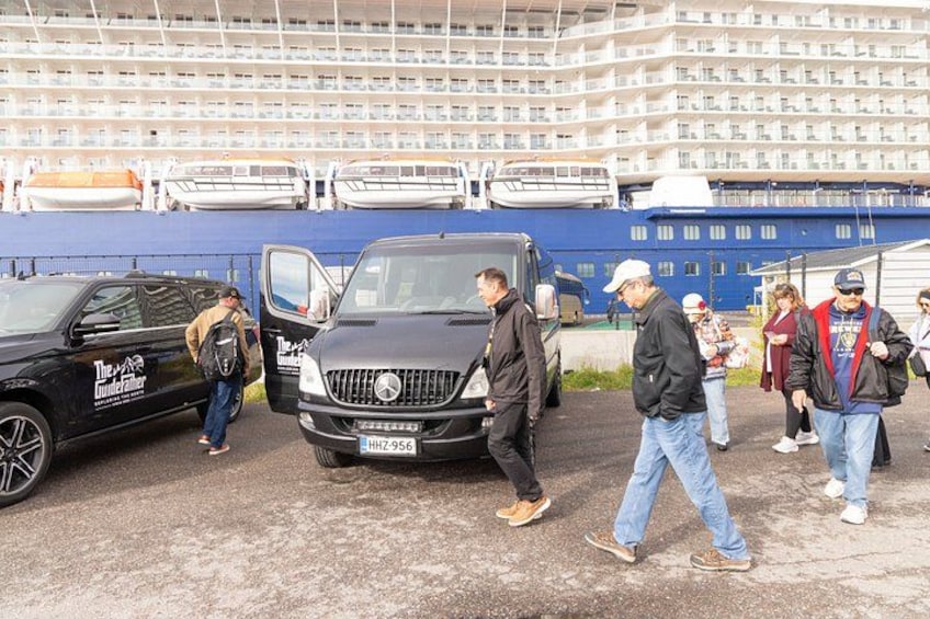 En gruppe mennesker går nær en sort bil og en bus med en blå bygning i baggrunden. 3