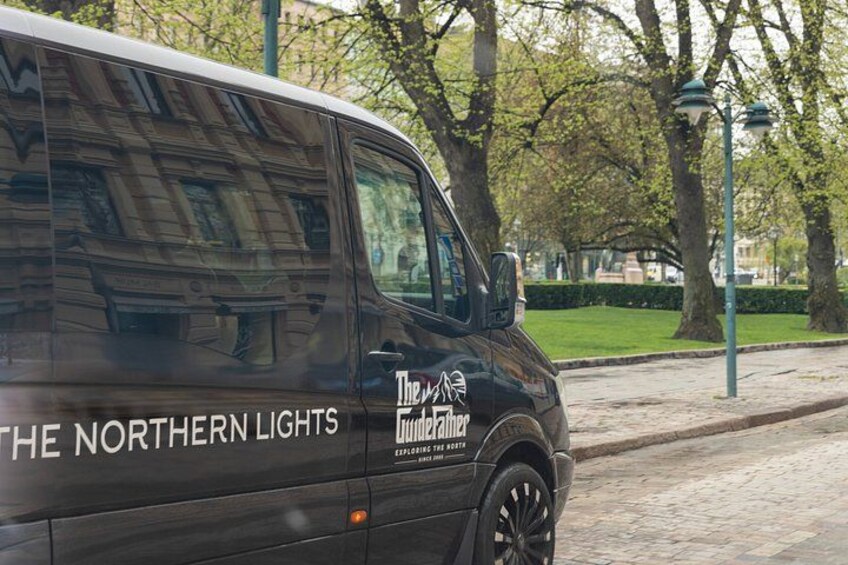 A black van parked on a cobblestone street with trees and a lamppost in the background. 3