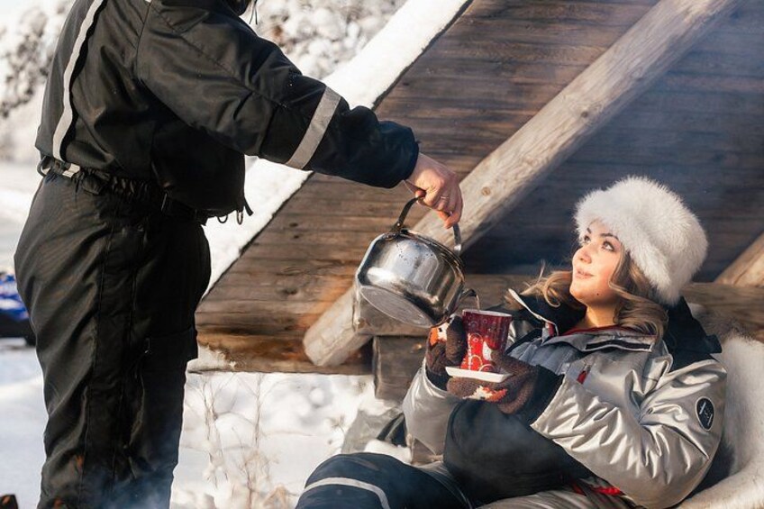 A person pouring a hot beverage into a cup held by another individual in a snowy outdoor setting. 1