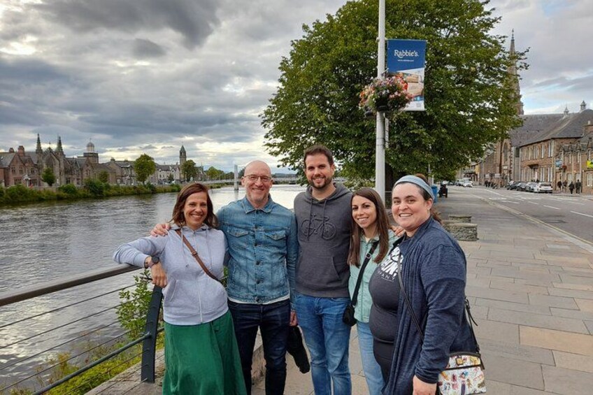 Un grupo de personas de pie junto a un río, con edificios históricos al fondo. 4