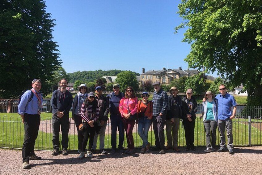 A group of people standing in a park with a building in the background. 2