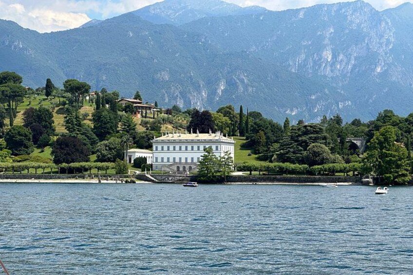 Un lago con un edificio blanco grande rodeado de follaje y montañas al fondo. 4