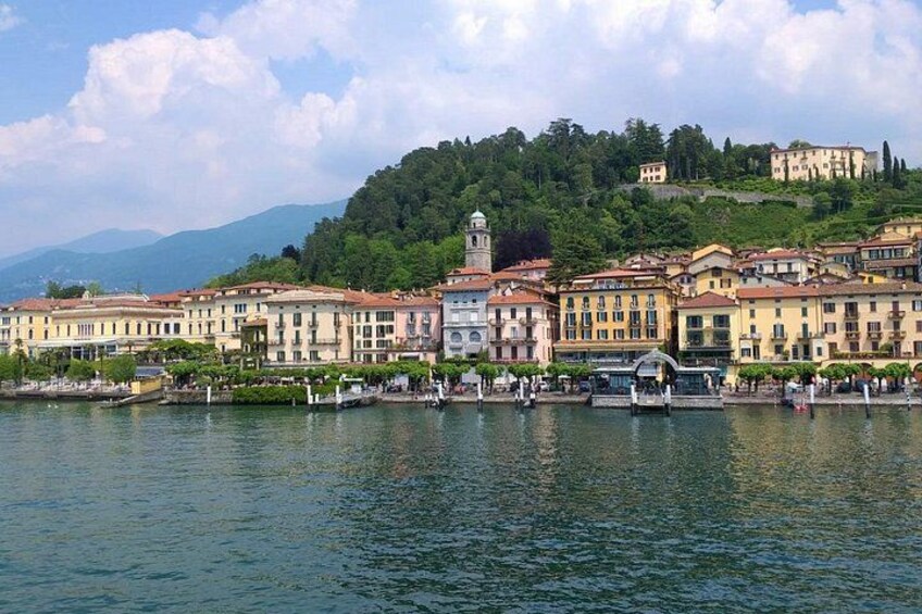 Un pueblo a orillas de un lago con edificios históricos, una torre destacada y una colina con vegetación al fondo. 5