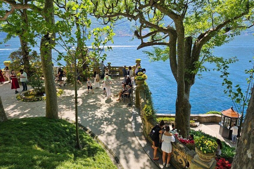 Un paseo marítimo junto al lago con gente caminando, árboles y un pabellón. 2