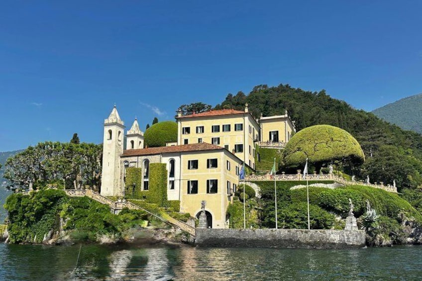 A historic building with a tower, a dome-shaped tree, and a lake. 1