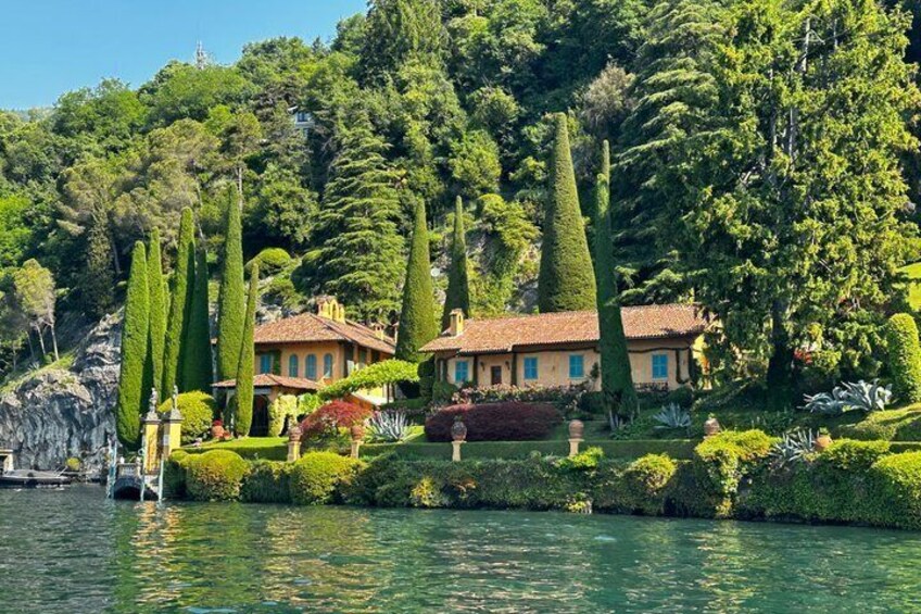 A lakeside villa with manicured gardens, tall cypress trees, and a clear view of the water. 2