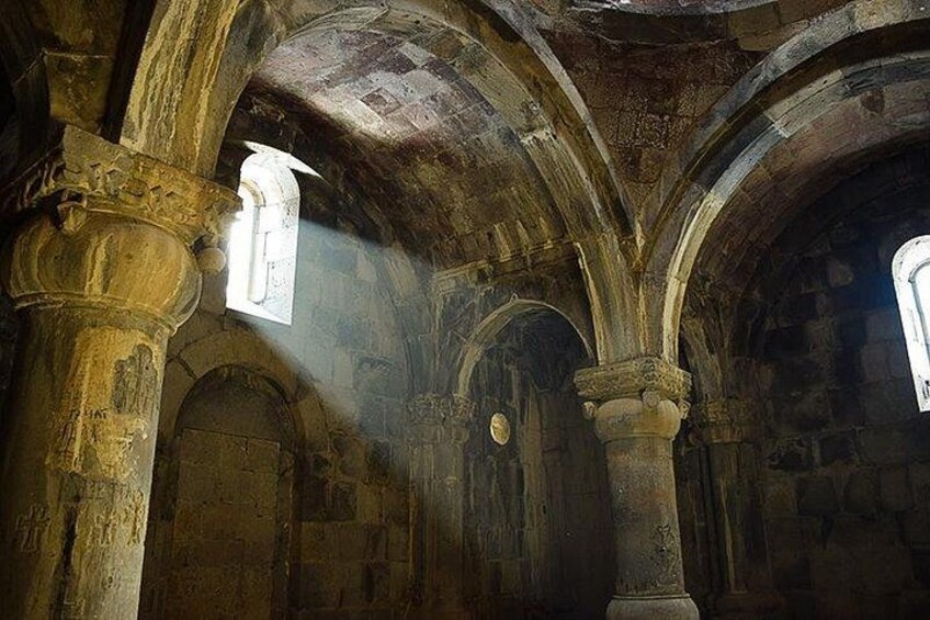 An interior of a historical building with arched ceilings, stone columns, and a small window allowing light to enter. 4