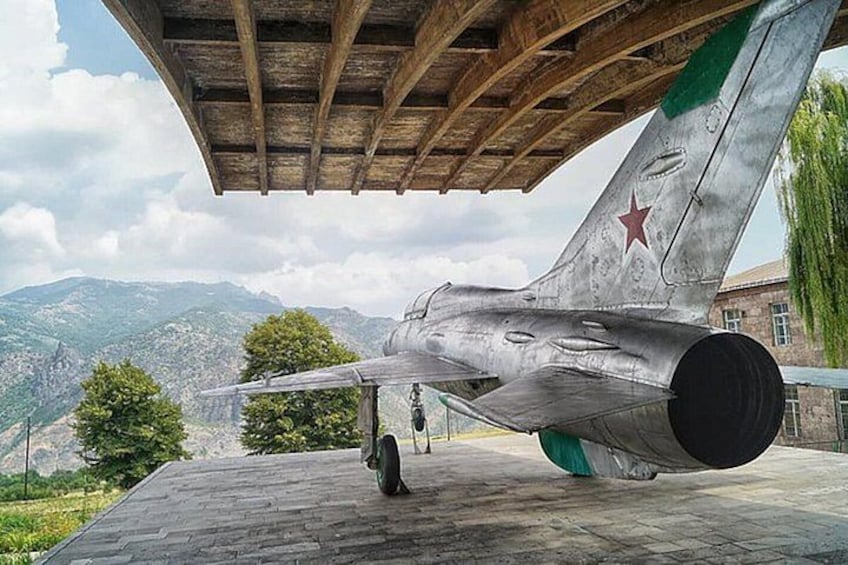 Un avión militar con una insignia de estrella en la cola, estacionado sobre una superficie pavimentada frente a un paisaje montañoso. 1