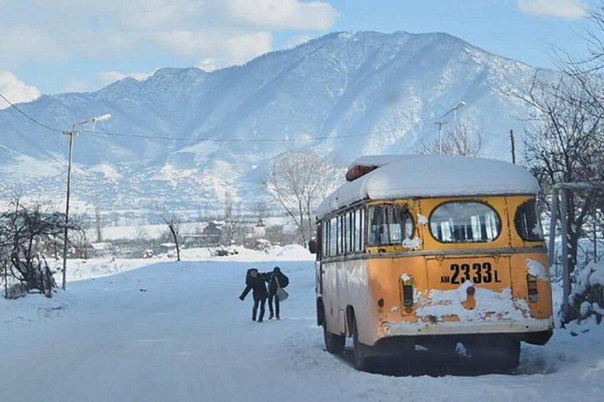 A yellow bus with the number 2333L parked on a snow-covered road with mountains in the background. 2