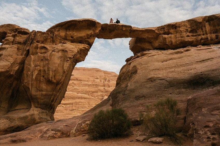 A natural rock arch formation with two people standing on top. 3