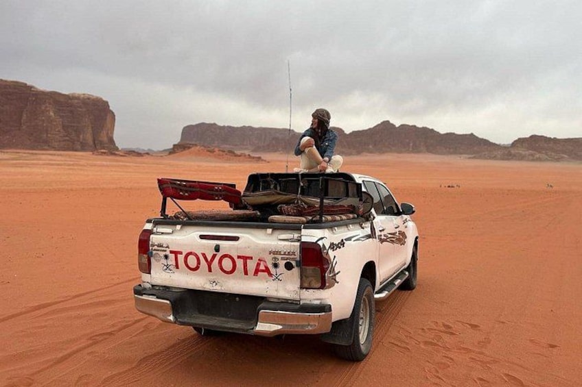 A white Toyota pickup truck in a desert with a person sitting on the back. 3
