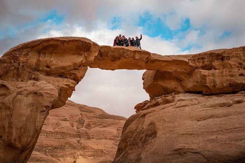 A group of people standing on a natural rock arch formation. 2