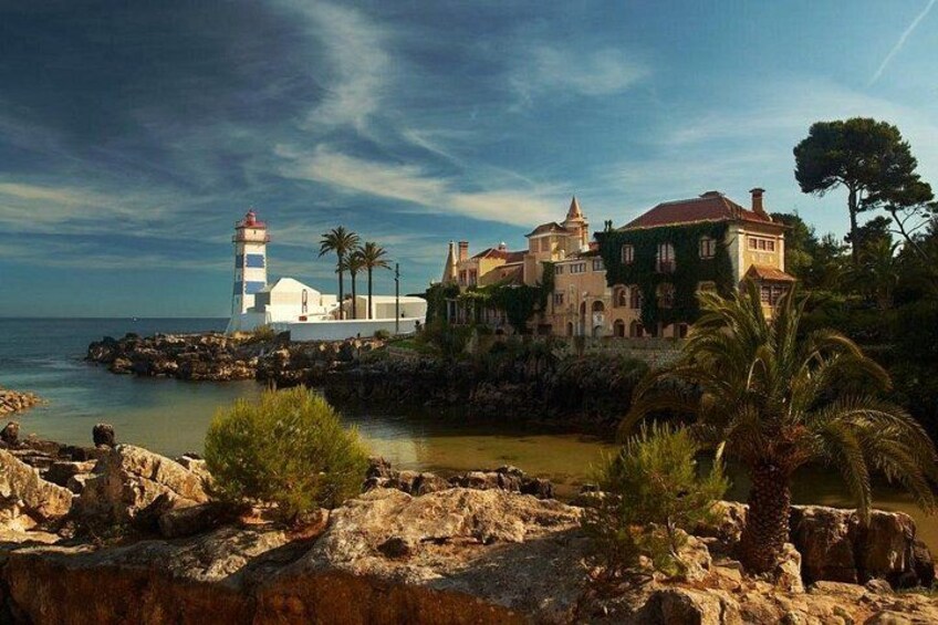 A coastal landscape with a lighthouse, a large house with a red roof, and rocky terrain. 5