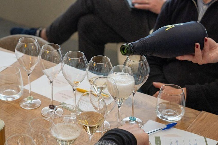 A person pouring a liquid from a bottle into a wine glass on a table with several other glasses and a menu. 2