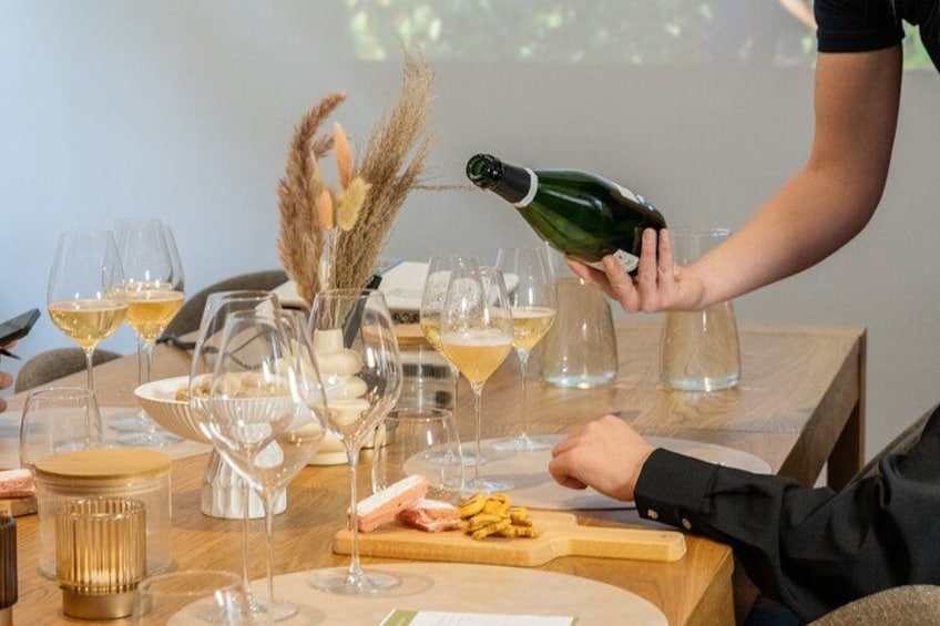 Une table à manger avec des verres à vin, une bouteille de vin dont on verse le contenu, et une assiette de nourriture. 2