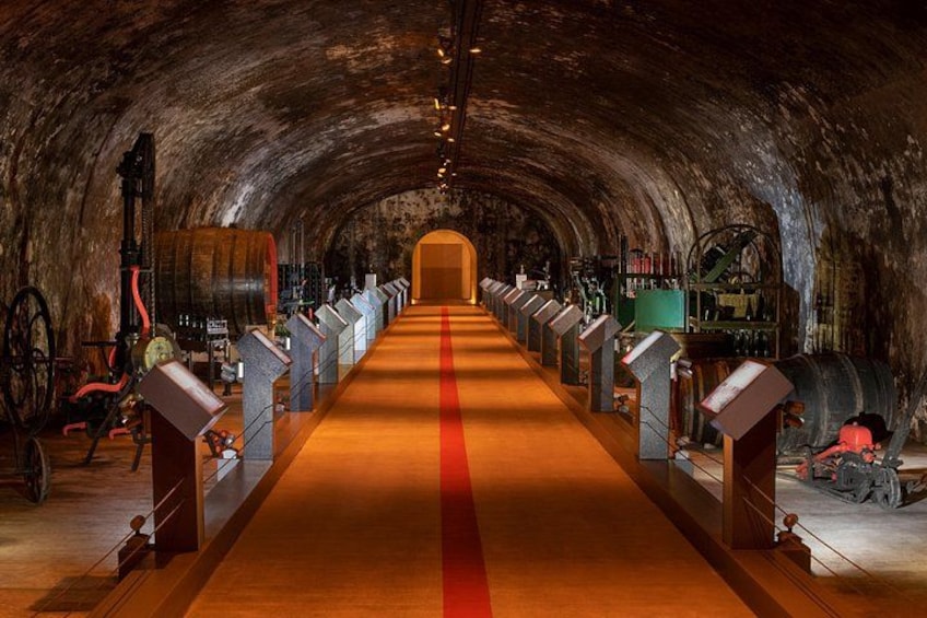 A long, dimly lit tunnel with a red carpet, wooden barrels, and metal machinery. 2