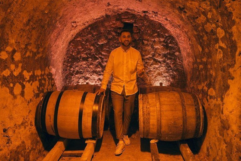 A person standing between two wooden barrels in a tunnel with rough, textured walls. 2