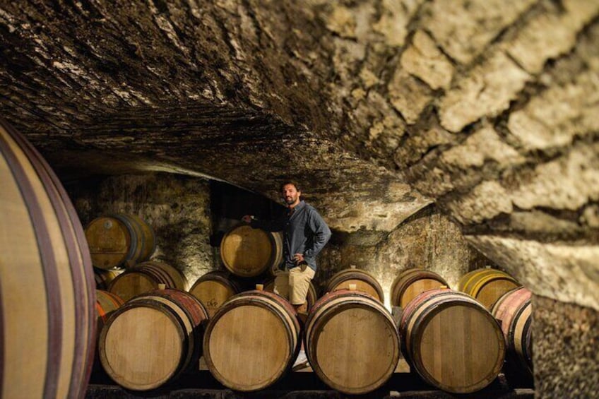 A man standing among wooden wine barrels in a cellar. 1