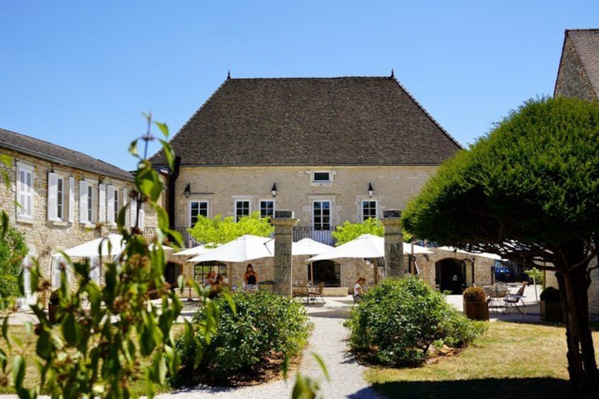 A stone building with a tiled roof, surrounded by a garden with white umbrellas and greenery. 2