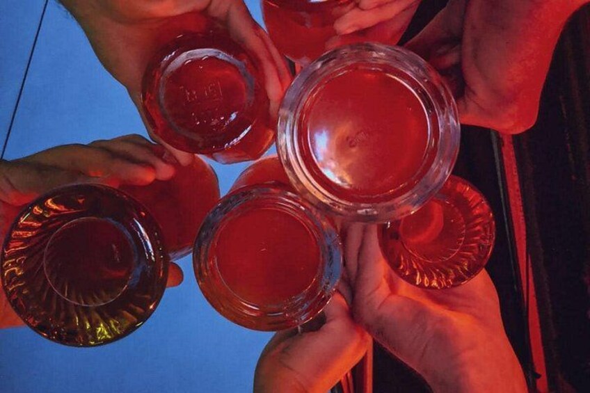 En grupp människor håller i genomskinliga glas som är fyllda med en röd vätska, troligen en dryck, och de befinner sig i en social miljö. 3