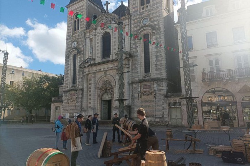 A historic stone building with a clock tower, surrounded by people and barrels. 3