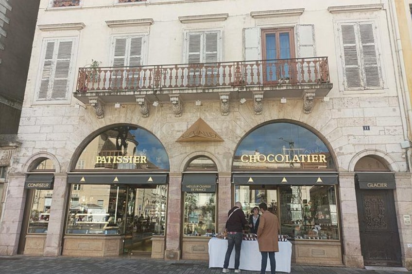 A building with storefronts labeled 'PATISSIER' and 'CHOCOLATIER' with people standing outside. 2