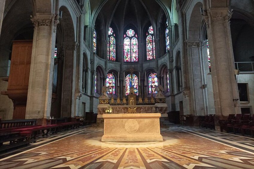 A cathedral interior with stained glass windows, a central altar, and a patterned floor. 3