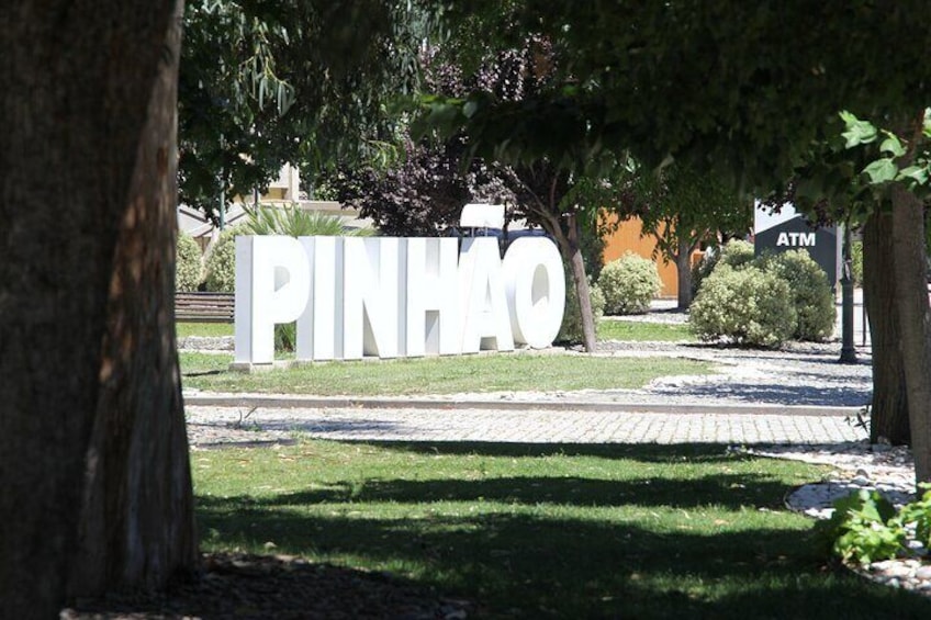 Un letrero blanco grande con la palabra "PINHAO" al frente, rodeado de árboles y un sendero pavimentado. 3