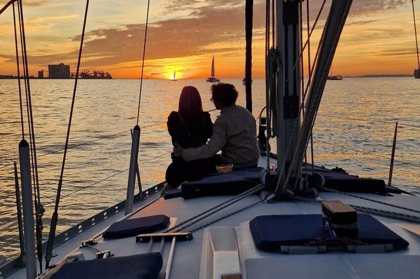 A couple on a sailboat during sunset with the sun setting on the horizon. 3